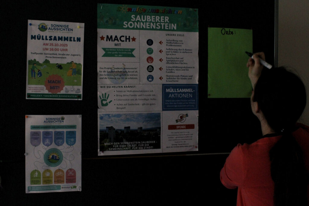 Eine Person steht vor einer Tafel mit Informationen zur Müllsammelaktion für Nachbarschaft und Demokratie in Pirna-Sonnenstein.