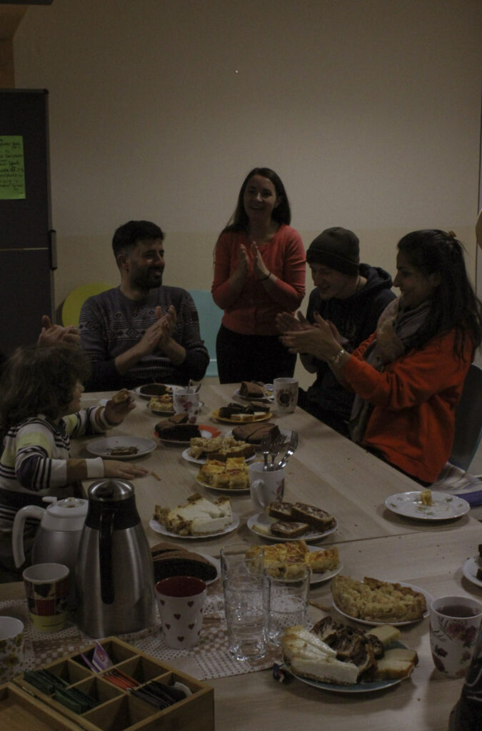 Teilnehmer*innen sitzen bei Kaffee und Kuchen nach einer Nachbarschaftsaktion zusammen und applaudieren