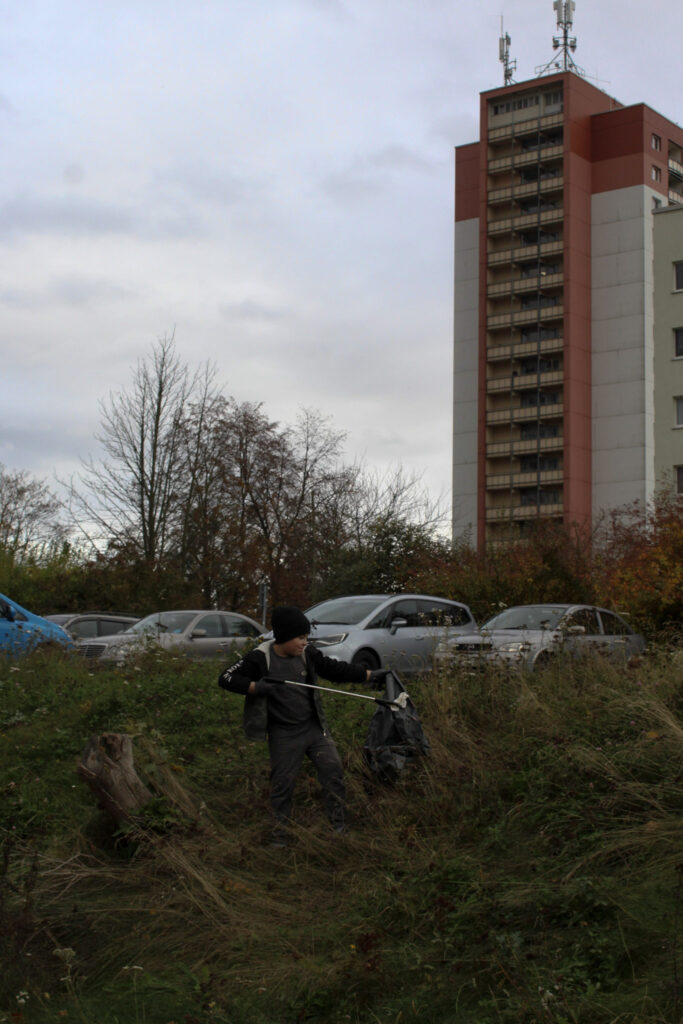 Ein Junge steht sammel Müll bei eienr Nachbarschaftsaktion in Pirna, im Hintergrund sieht man einen für den sonnenstein typischen Plattenbau.