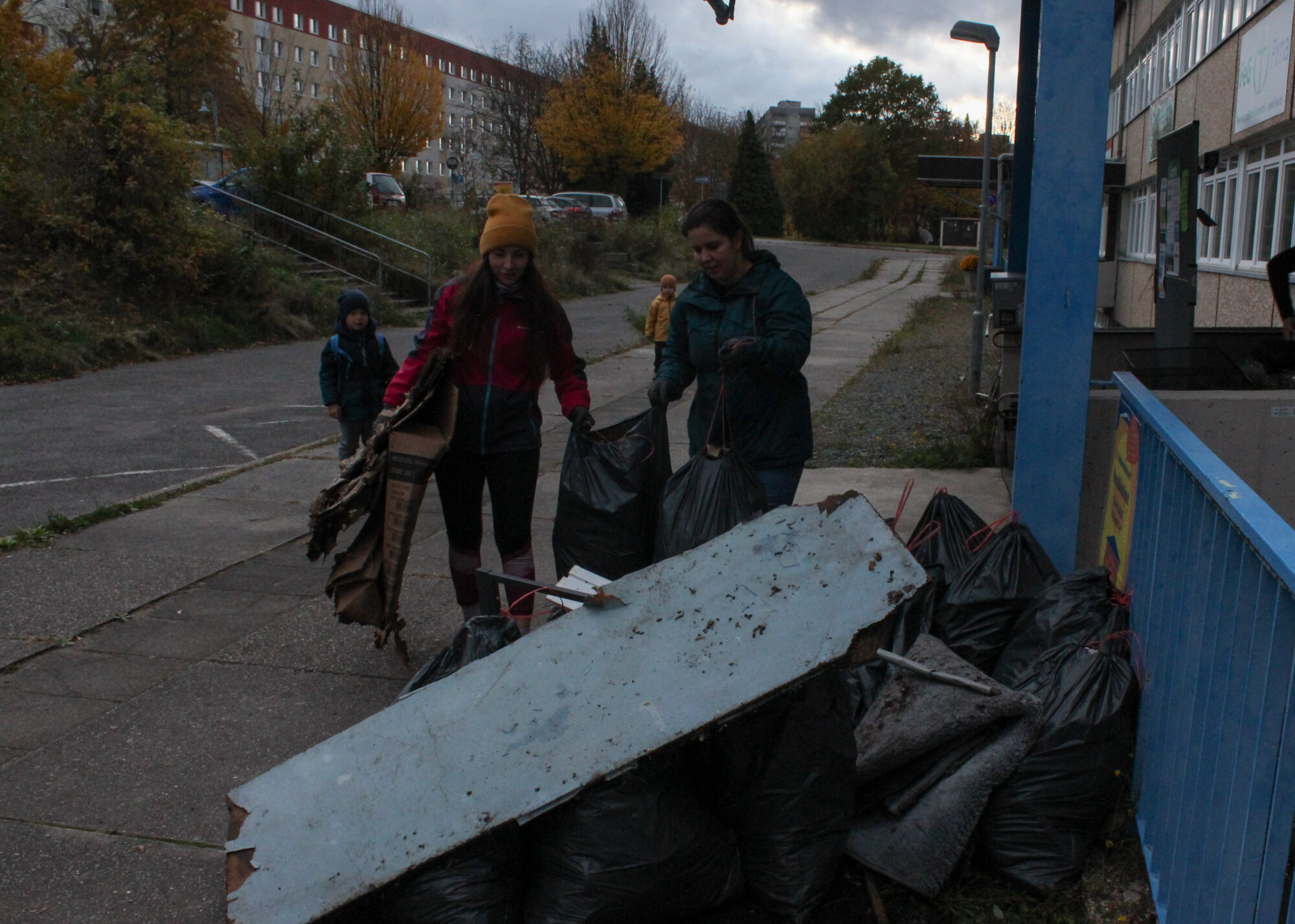 Bewohner*innen sammlen Müll in der Nachbarschaft, im Vordergrund sieht die vollen Müllsäcke gestapelt.