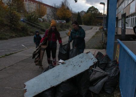 Bewohner*innen sammlen Müll in der Nachbarschaft, im Vordergrund sieht die vollen Müllsäcke gestapelt.