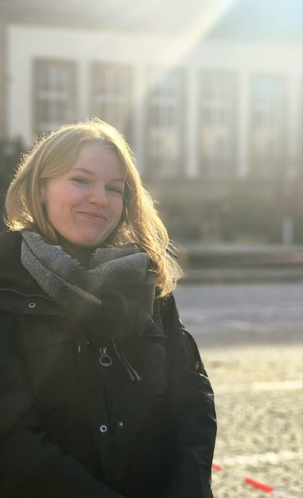 Eine junge Frau steht mit Gegenlicht und tiefer Sonne vor dem Koblenz-Kolleg.